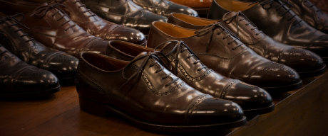 暗い照明の中で、たくさんの茶色と黒の革靴が整然と並べられている様子。