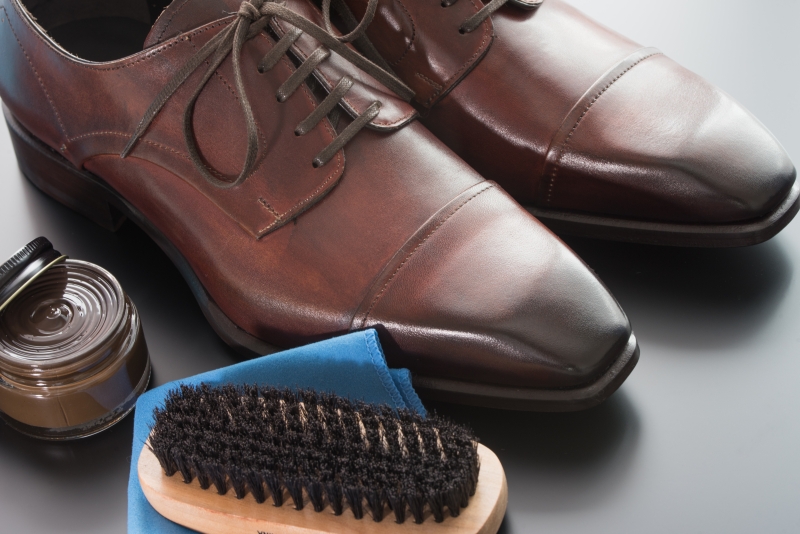 艶やかに磨かれた茶色の革靴と、シューケアに必要な靴クリーム、ブラシ、クロス。革靴の適切な手入れによる美しい仕上がりを示す